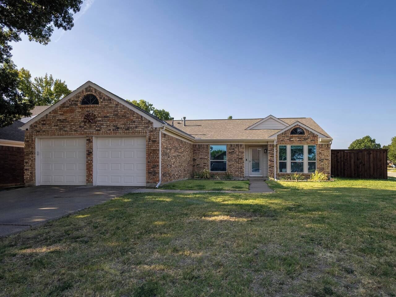 A two-story brick house with a garage, a front porch, and a fenced backyard.