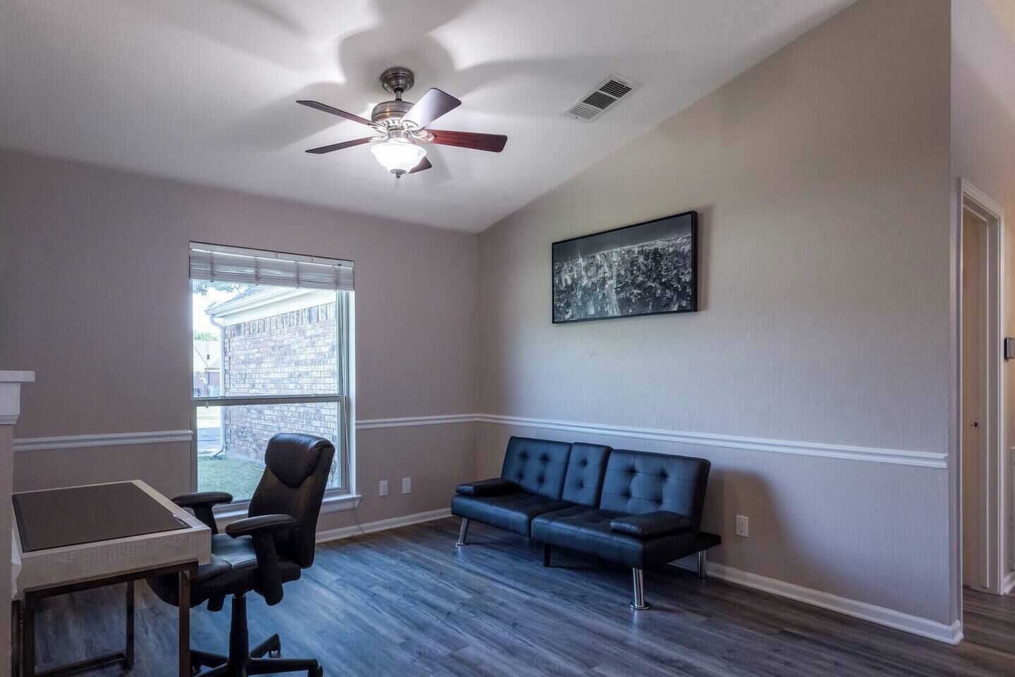 A room with a desk, office chair, blue sofa, and a ceiling fan.