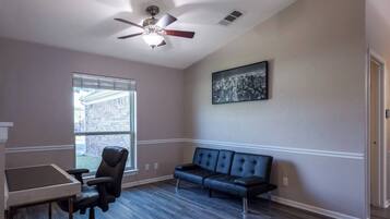 A room with a desk, office chair, blue sofa, and a ceiling fan.