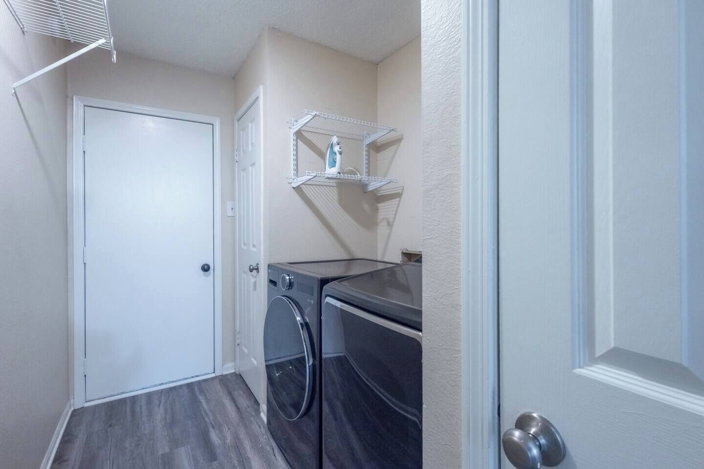 A laundry room with a door, two washing machines, and a shelf with an iron.