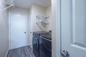 A laundry room with a door, two washing machines, and a shelf with an iron. - Family 3BR Gem with Private Pool & Game Room (Flower Mound)