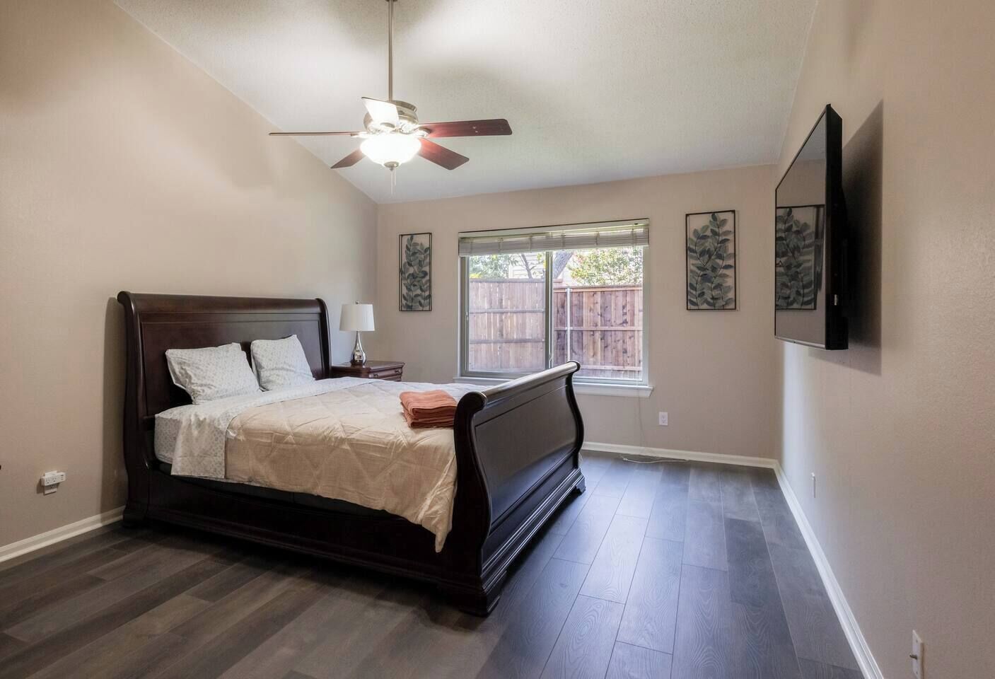 A bedroom with a bed, a ceiling fan, a window, and artwork on the wall.