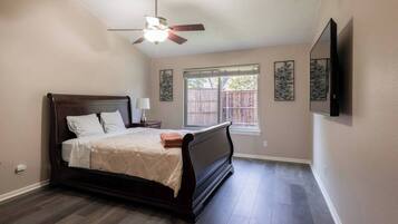 A bedroom with a bed, a ceiling fan, a window, and artwork on the wall.