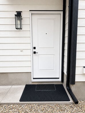 A white door with a black doorknob, a black mailbox, and a black doormat on a concrete step. - Le Crib home (Calgary)