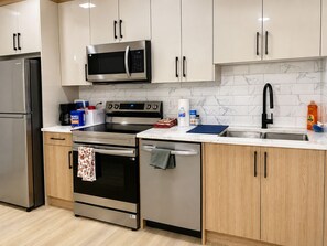A modern kitchen with stainless steel appliances, a microwave, oven, and dishwasher. - Le Crib home (Calgary)