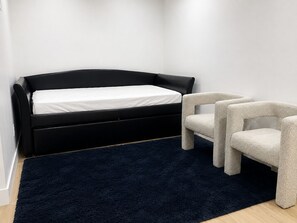 Een kamer met een zwart slaapbank, een witte stoel en een donkerblauwe vloerkleed.