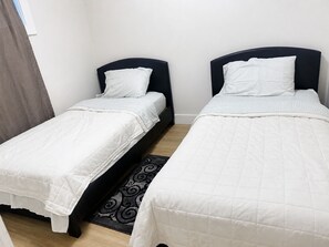 Two single beds with headboards, white bedding, and a patterned rug on a wooden floor. - Le Crib home (Calgary)