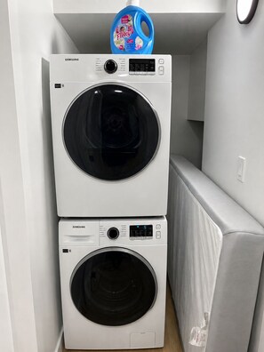 Two stacked Samsung washing machines in a laundry room with a white wall and a light switch. - Le Crib home (Calgary)