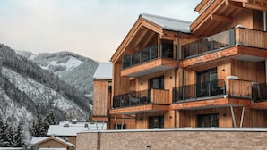 Ein mehrstöckiges Holzgebäude mit Balkonen vor einer verschneiten Berglandschaft.