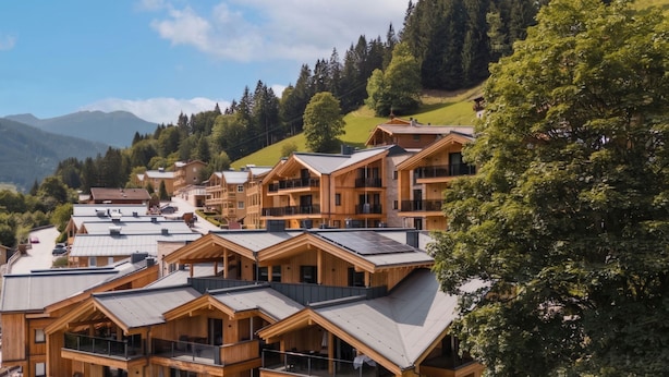 Eine Gruppe von Holzhäusern im Chalet-Stil mit Balkonen, vor dem Hintergrund grüner Hügel und eines klaren Himmels.