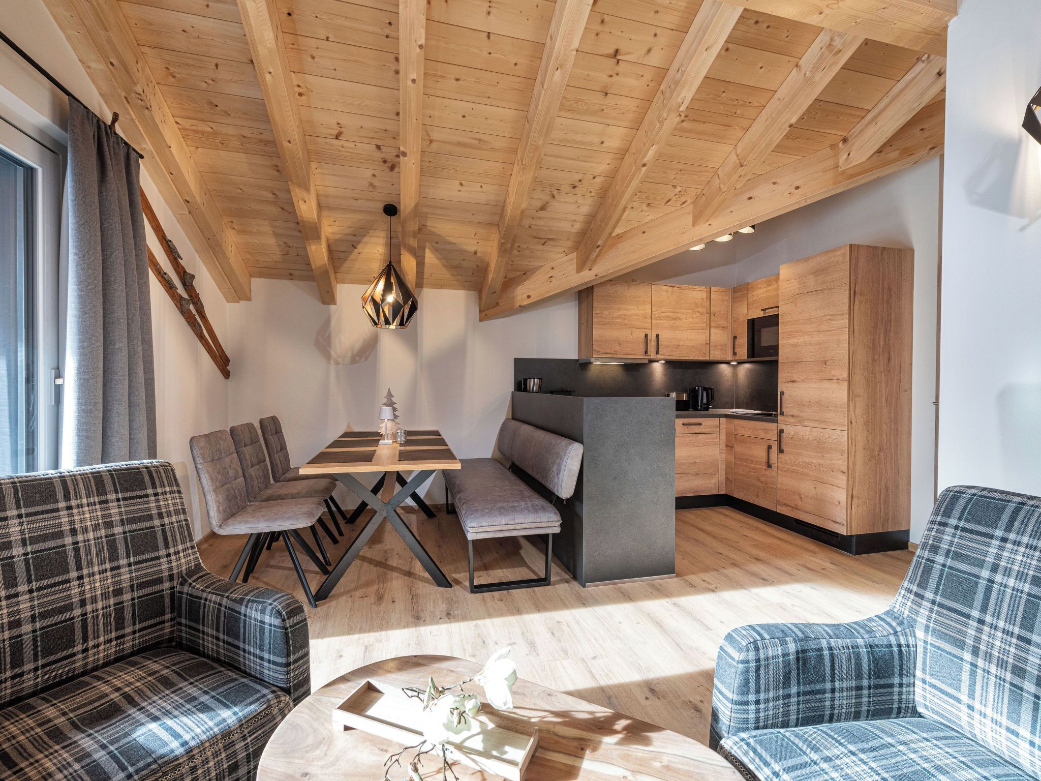 A modern interior with a wooden ceiling, a dining area with a table and chairs, a sofa, and a kitchen with wooden cabinets.