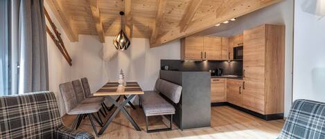A modern interior with a wooden ceiling, a dining area with a table and chairs, a sofa, and a kitchen with wooden cabinets.