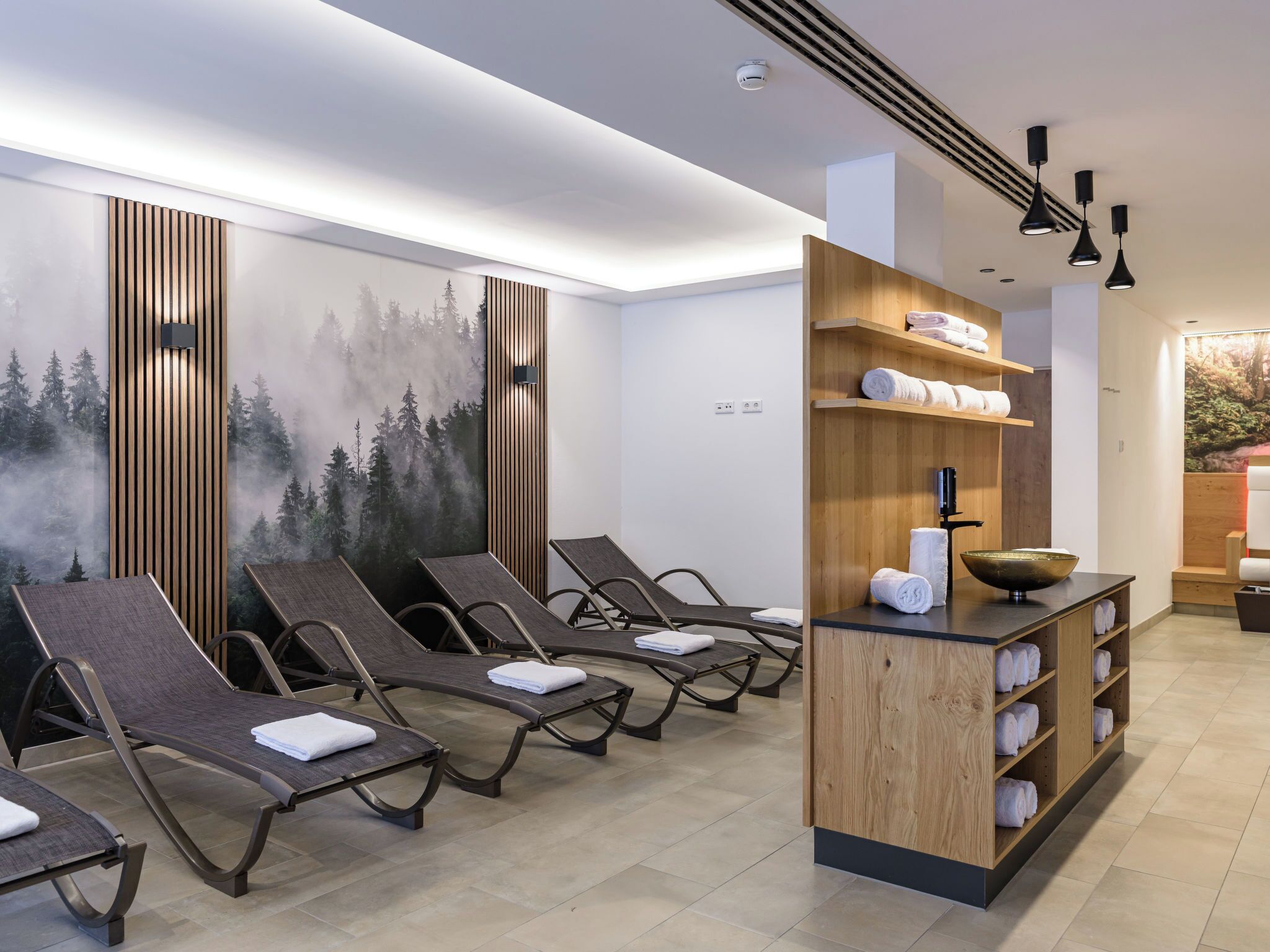 Ein Wellnessraum mit Liegesesseln, einer Holzeinrichtung mit Handtüchern und einem Wandgemälde.