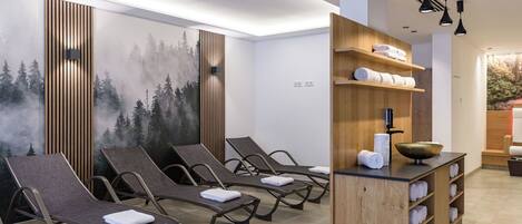 A spa room with reclining chairs, a wooden cabinet with towels, and a wall mural.
