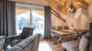 Ein modernes Interieur mit Holzboden, einem Esstisch mit Stühlen und Blick auf eine verschneite Landschaft durch große Fenster.