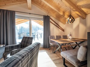 Un interior moderno con techo de madera, una mesa de comedor con sillas y vista a un paisaje nevado a través de amplios ventanales.