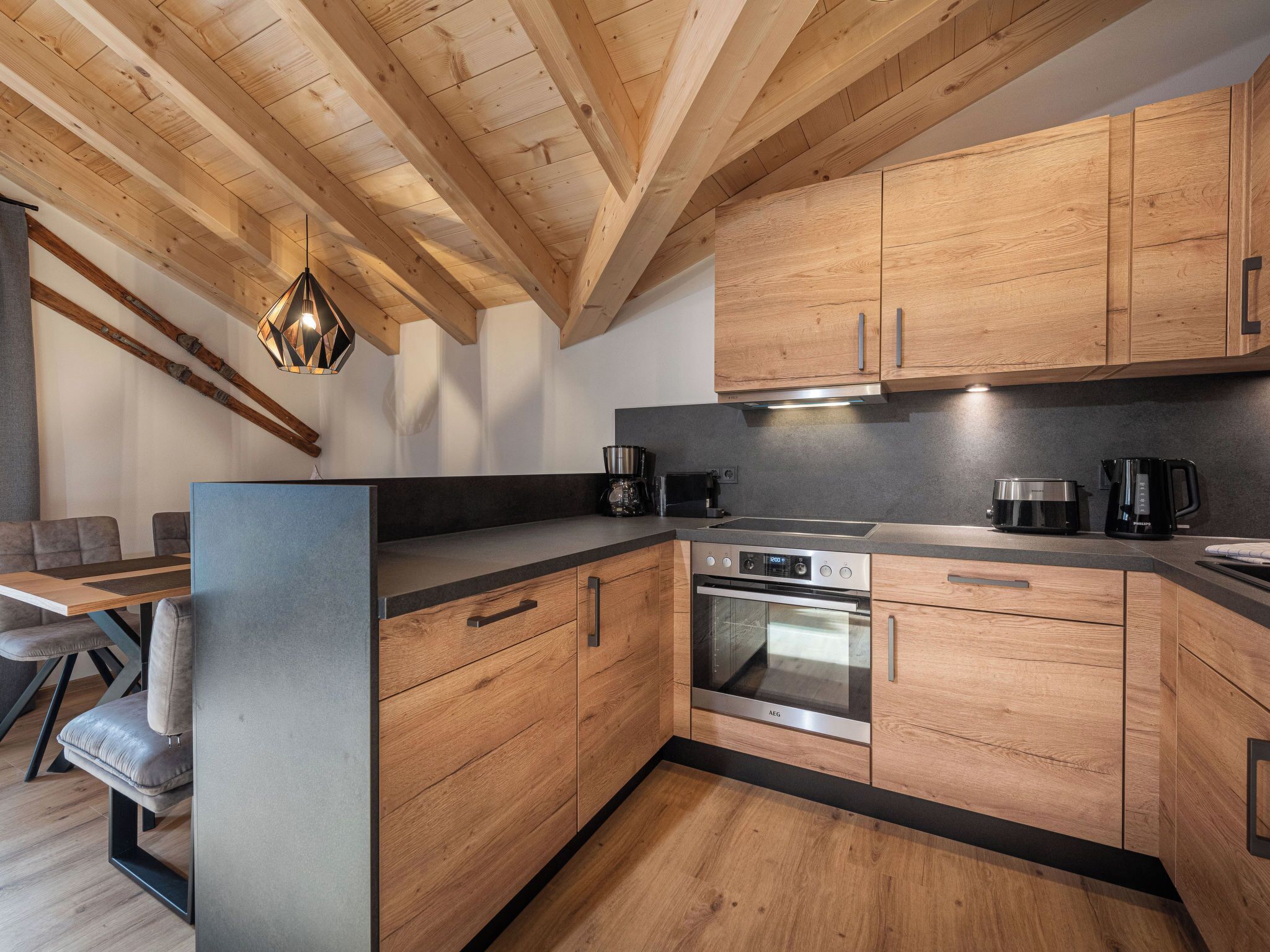 A modern kitchen with wooden cabinets, a built-in oven, and a dining area with a table and chairs.