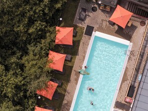 Eine Vogelperspektive auf einen Swimmingpool mit umliegenden Liegebereichen und einer dichten Baumgrenze.