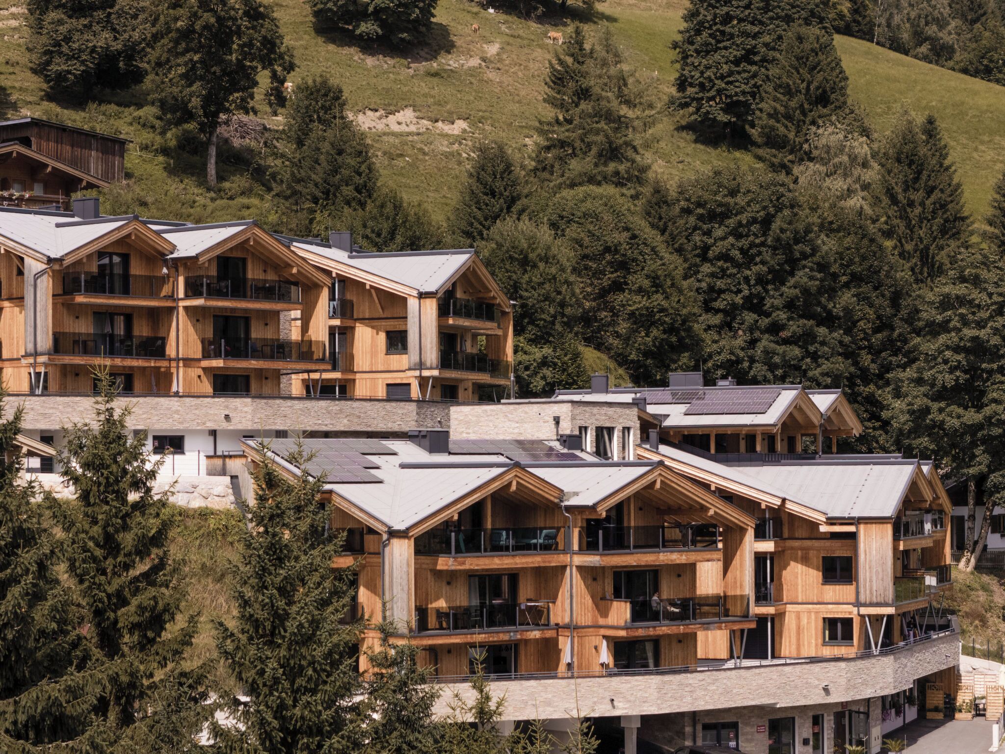 A multi-story wooden hotel with balconies and large windows, surrounded by trees and a hilly landscape.