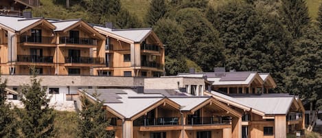 A multi-story wooden hotel with balconies and large windows, surrounded by trees and a hilly landscape.