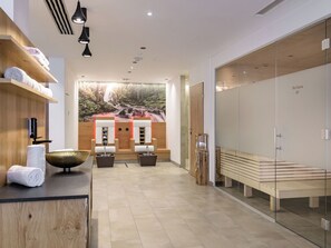 Un moderno spa con un mostrador de recepción de madera, un mural grande con una cascada y una zona de sauna con bancos.