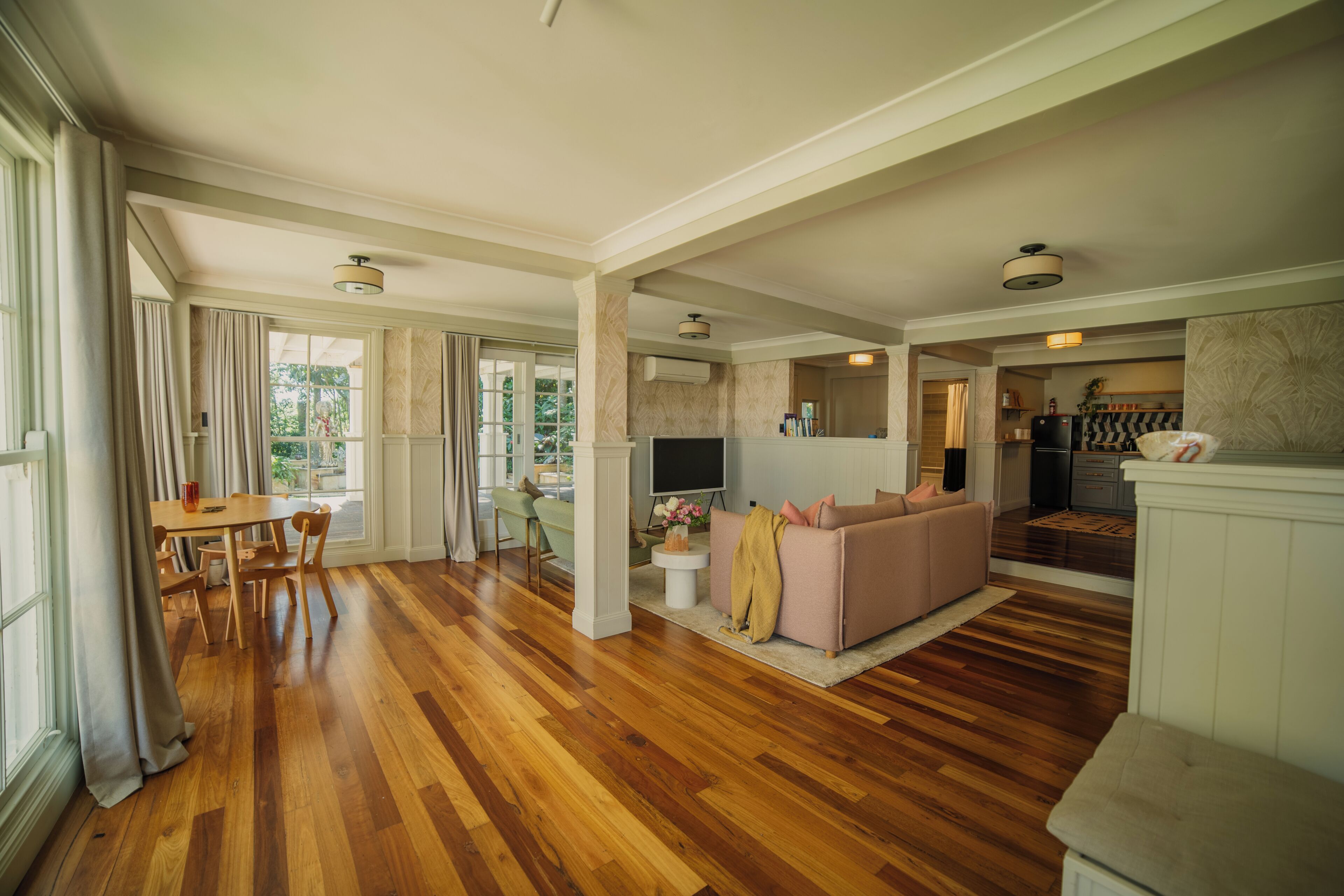A spacious living area with hardwood flooring, a sofa, a dining table with chairs, and a kitchen area visible through an open doorway.