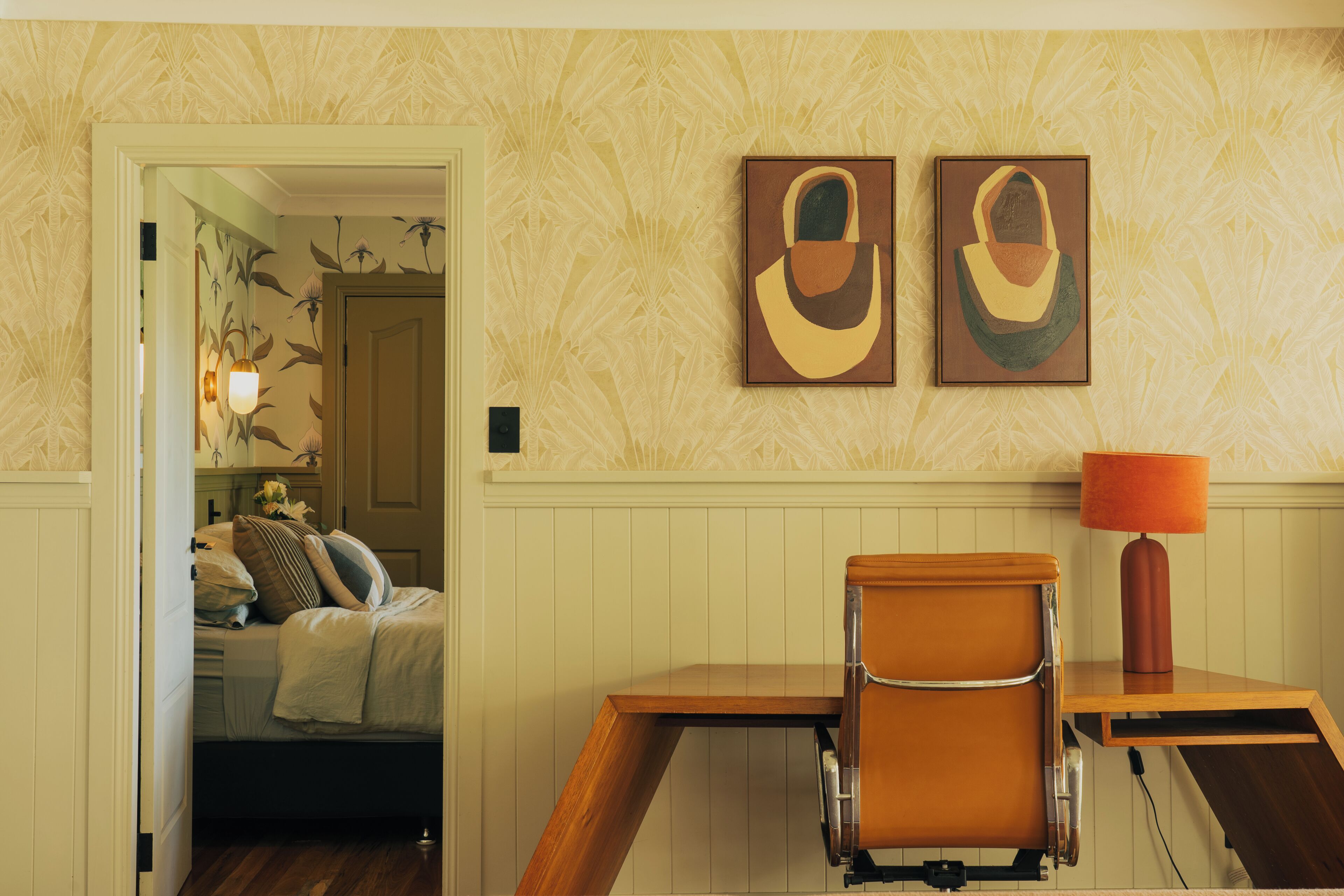A room with a bed, a desk, a chair, and two wall-mounted paintings.