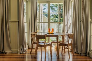 Un coin repas avec une table ronde, des chaises en bois et une vue par une fenêtre ornée de rideaux.
