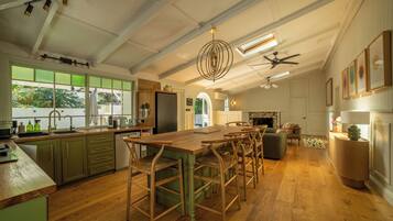 A spacious kitchen with a large wooden table and bar stools, a built-in oven, and a window overlooking greenery.