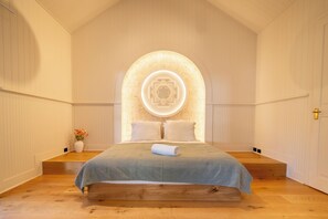 Une chambre à coucher avec un lit, une table de chevet, un vase avec des fleurs et un luminaire fixé au mur.