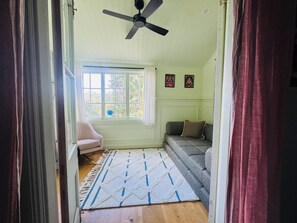 Una habitación con ventilador de techo, una ventana con cortinas, un sofá, una silla y un tapete estampado.