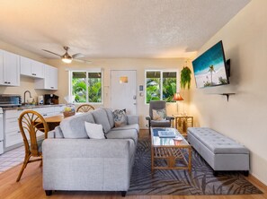 A compact living space with a kitchenette, a sofa, a dining table, and a TV mounted on the wall. - Oceanfront 1/1 Kailua Kona Shores | Lanai + Pool (Kailua-Kona)