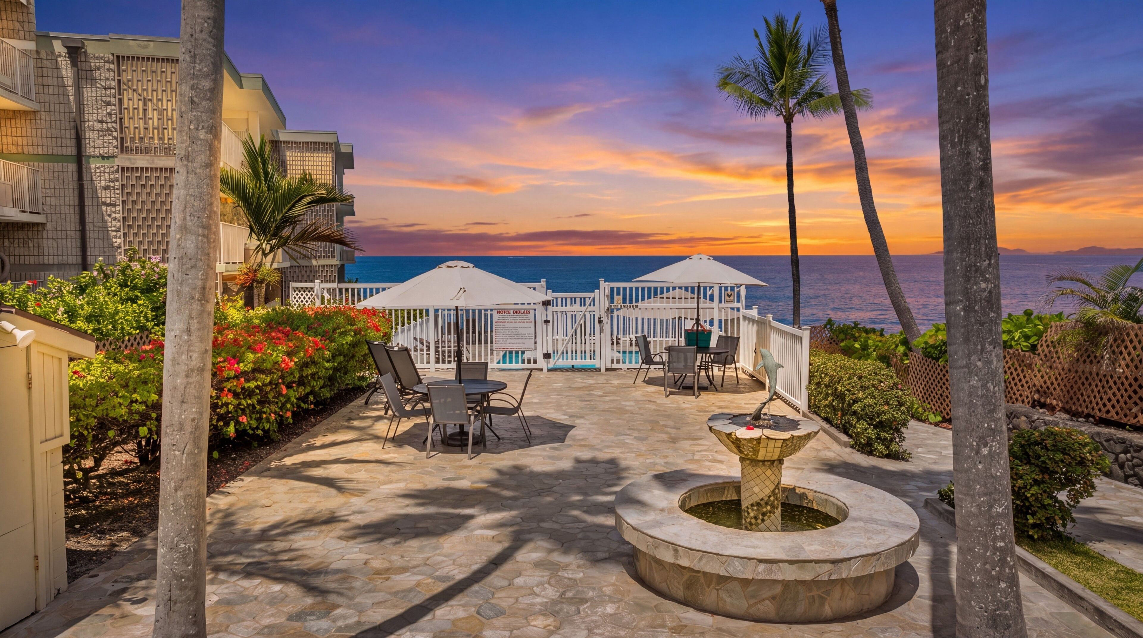 Un patio de resort con mobiliario exterior, piscina y vista al océano al atardecer.