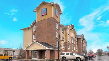 A multi-story hotel with a prominent '6' sign on the facade, a covered entrance, and a parking lot with several vehicles.