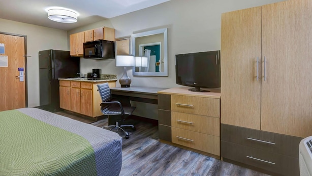 A hotel room with a bed, a desk with a computer, a TV, a microwave, and a refrigerator. - Extended Stay Studio w/ Kitchenette | Town Center Plaza - 6.7 miles (Johnson County)