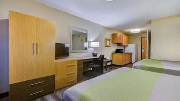 A hotel room with two beds, a desk, a chair, a television, and a kitchenette.