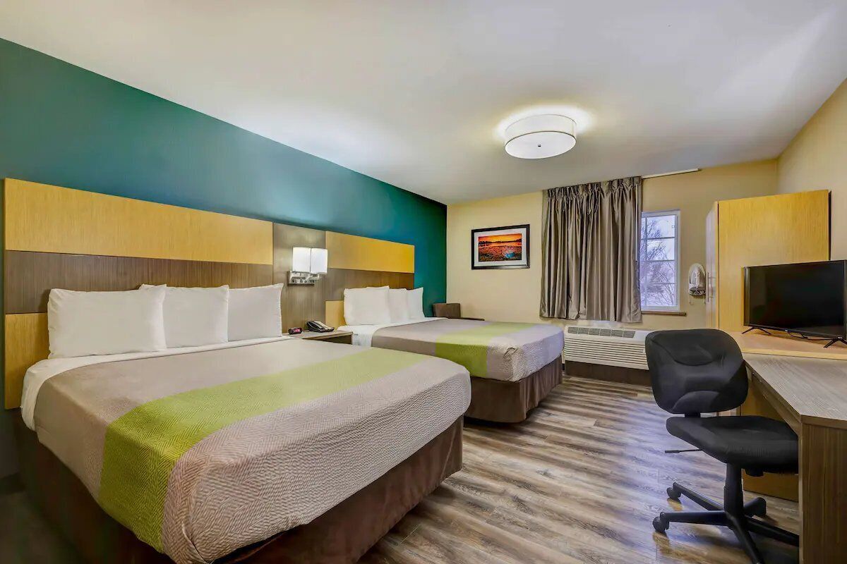 A hotel room with two beds, a desk with a chair, a television, and a window with curtains.