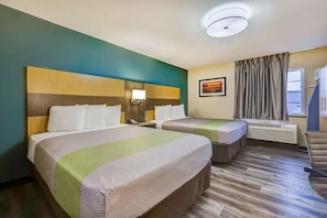 Hotellihuone, jossa on kaksi sänkyä, työpöytä, tuoli, ikkuna verhoilla ja kattovalaisin.