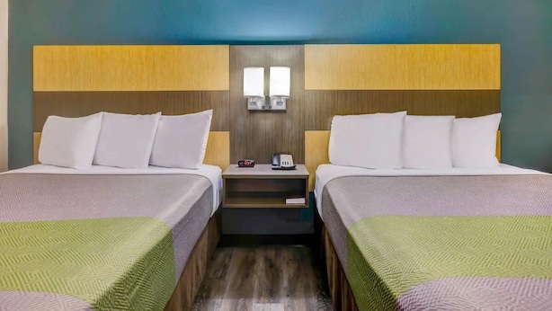 Ein Hotelzimmer mit zwei Betten, einem Nachttisch und einer wandmontierten Lampe.