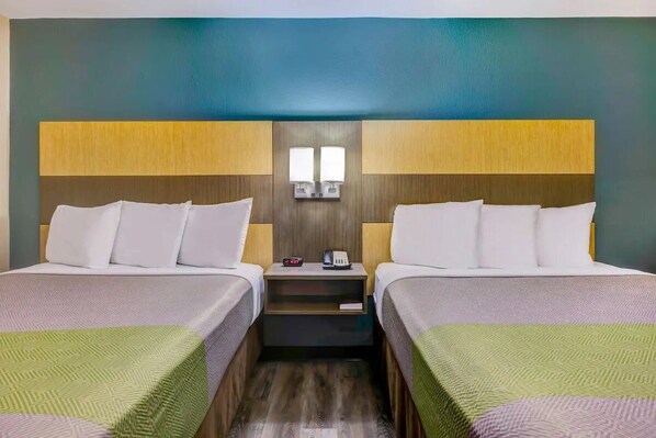 Hotellihuone, jossa on kaksi sänkyä, yöpöytä ja seinään kiinnitetty valaisin.