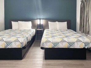 Una habitación de hotel con dos camas, una mesita de noche y una lámpara de pared.