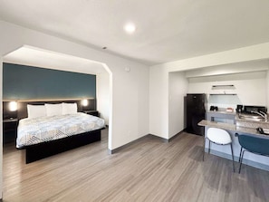 Una habitación de hotel moderna con cama, escritorio, silla, kitchenette y baño.