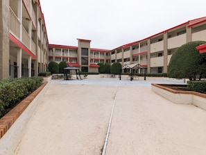 A courtyard with a covered seating area, a small kiosk, and a building with multiple balconies and a red roof. - Enjoy Affordable Comfort | 2 Units in Central Irving | Pet-Friendly Stay (Irving)