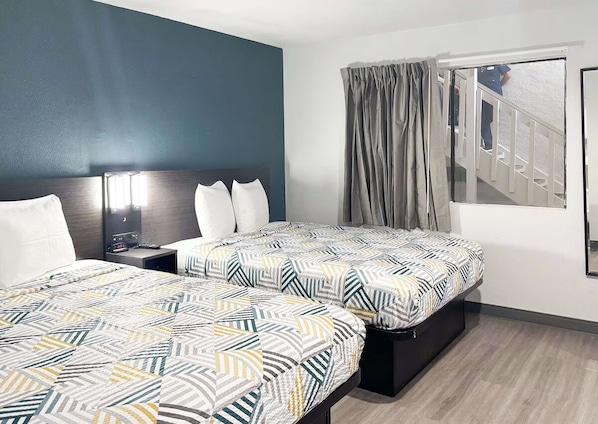 Habitación de hotel con dos camas, una mesita de noche, una ventana con cortinas y vista a una escalera.
