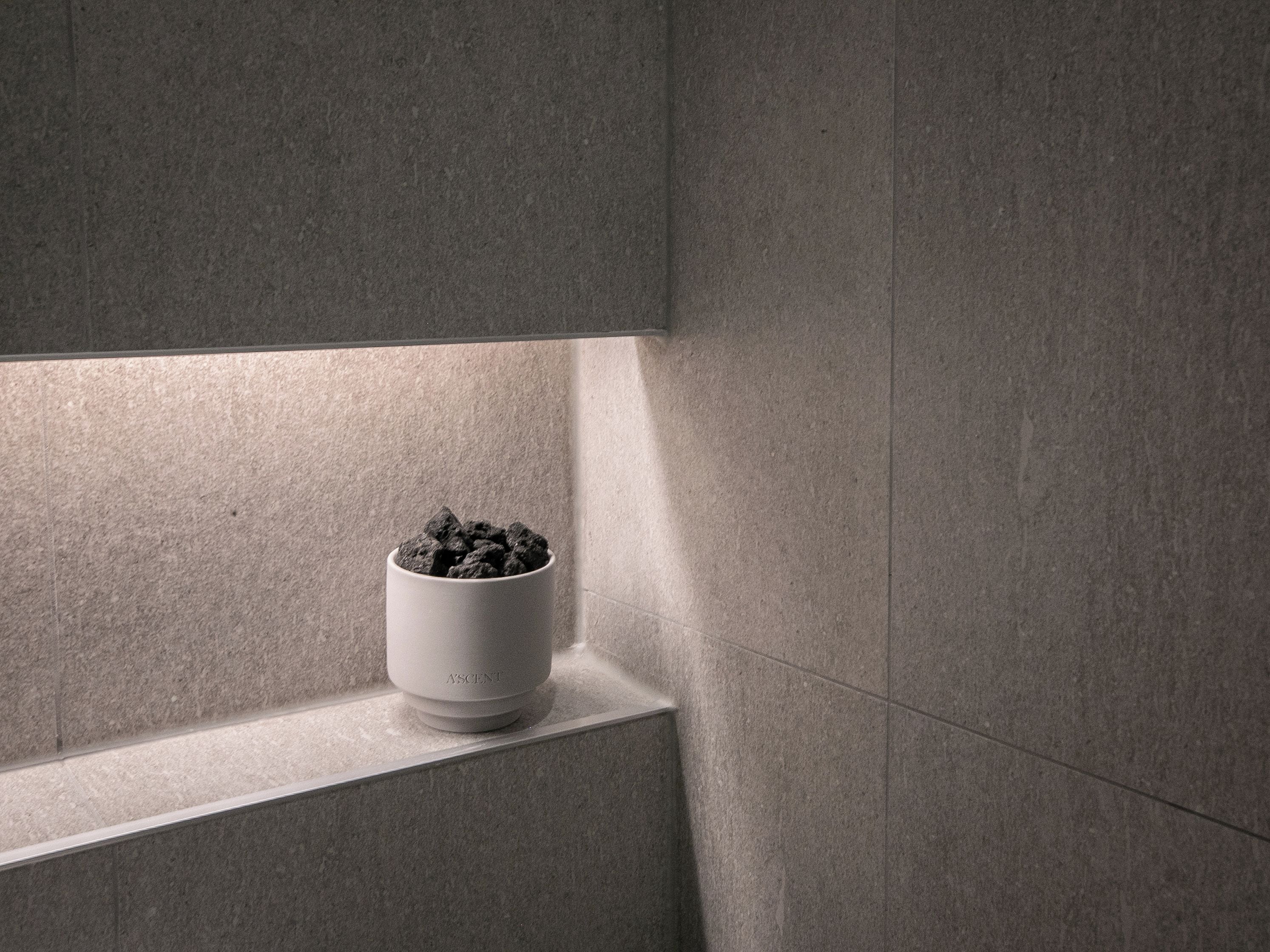 A white ceramic pot with a textured surface, placed on a ledge against a wall with a subtle texture.