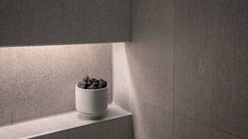A white ceramic pot with a textured surface, placed on a ledge against a wall with a subtle texture.