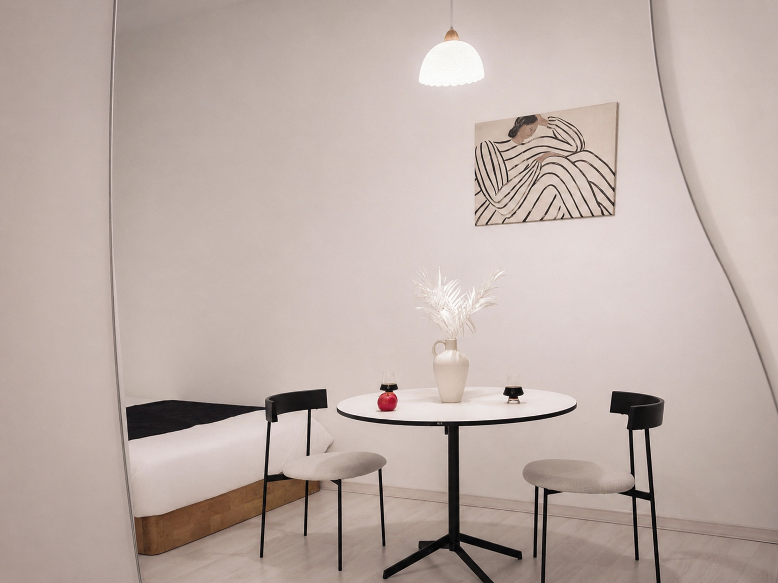 A modern room with a white sofa, a round table with chairs, a vase with white flowers, and a pendant light.