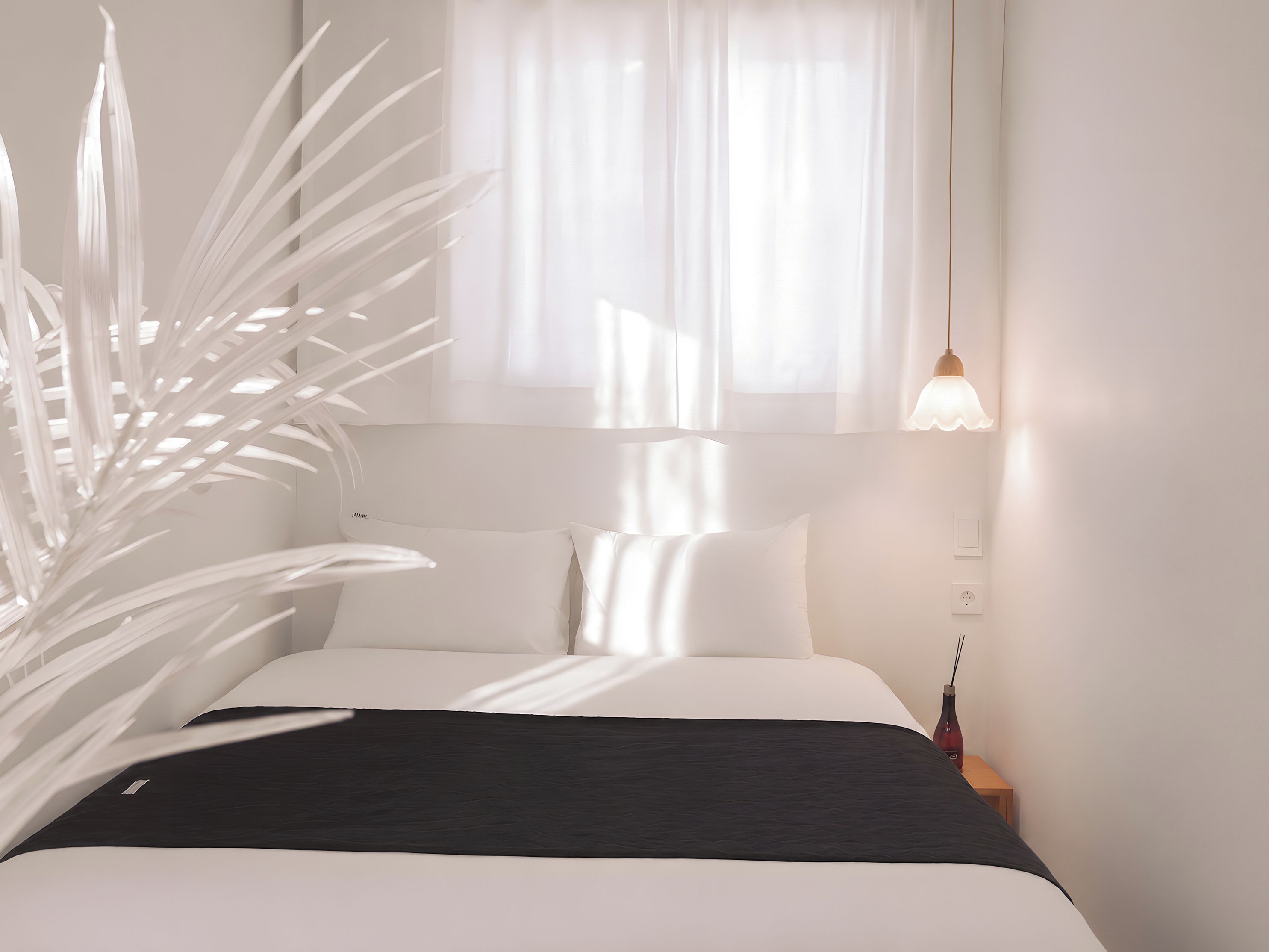 A bed with white bedding, a dark headboard, and a bedside table with a lamp.