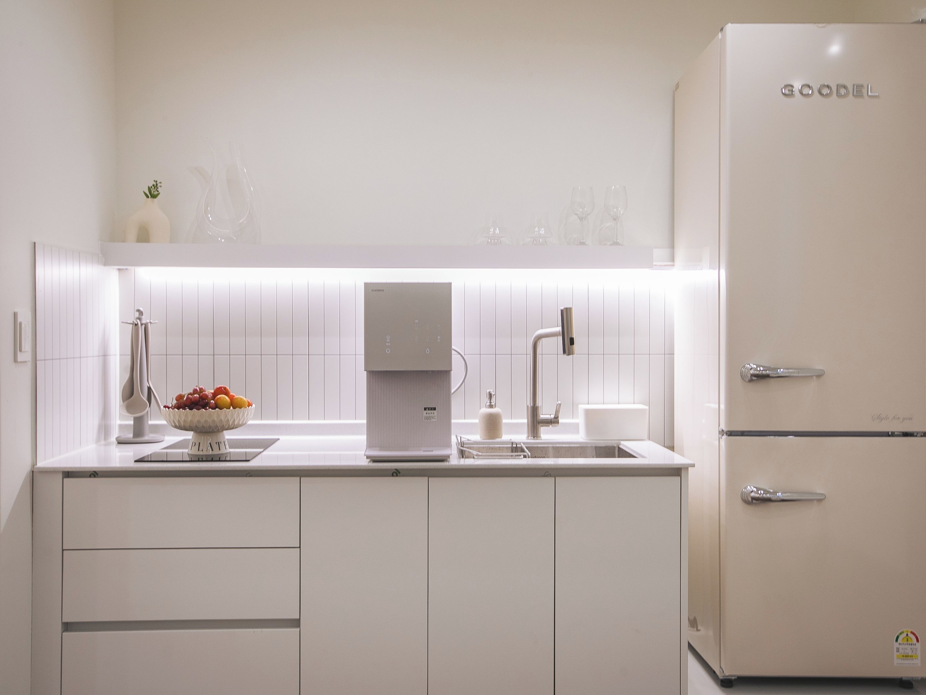 A modern kitchen with white cabinetry, a built-in coffee maker, and a fruit bowl on the counter.