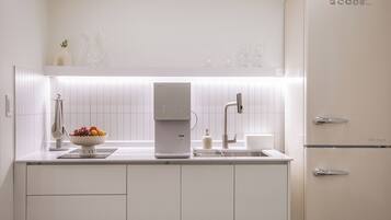 A modern kitchen with white cabinetry, a built-in coffee maker, and a fruit bowl on the counter.